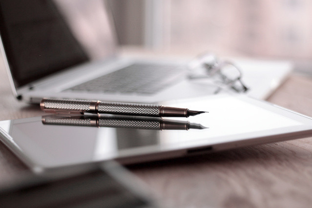 ein Kugelschreiber liegt auf einem Tablet und daneben liegt eine Brille auf einem Laptop 