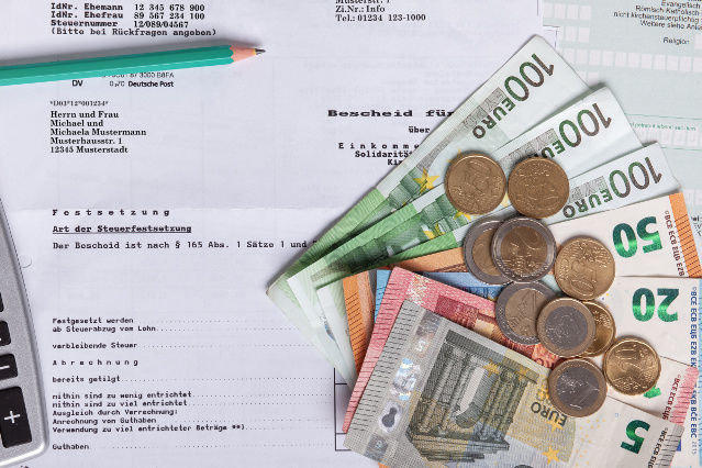 es ist ein Teil eines Steuerbescheides, Geldscheine und Münzen sowie ein Bleistift abgebildet (Quelle: ©hkmedia - stock.adobe.com) es ist ein Teil eines Steuerbescheides, Geldscheine und Münzen sowie ein Bleistift abgebildet