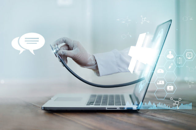 eine Hand hält ein Stethoskop und ragt aus dem Bildschirm eines Laptops, und um den Laptop sind digitale Gesundheitssymbole abgebildet (verweist auf: Selbstauskünfte)