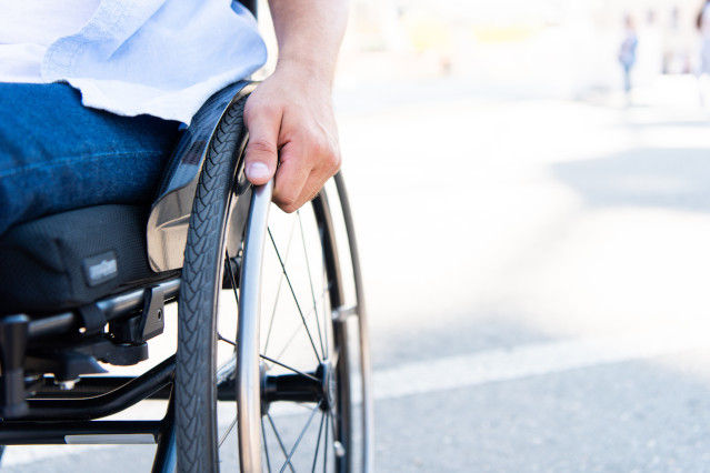 ein Mann sitzt im Rollstuhl und seine Hand fasst das Rollstuhlrad