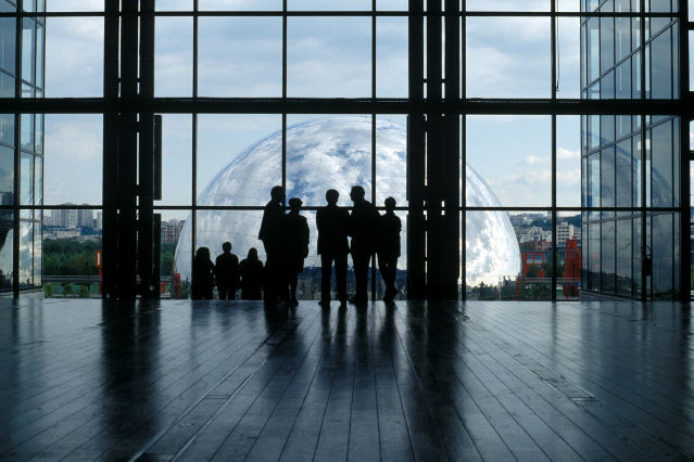 es sind Personen in einem Raum vor einer großen Glasfront abgebildet