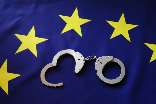 Handschellen liegen mitten im Sternkreis der EU-Flagge (verweist auf: Europäische Einrichtungen zur Strafverfolgung)