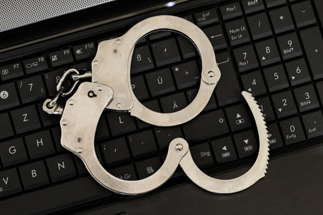 Handschellen liegen auf einer Computertastatur (verweist auf: Interpol)