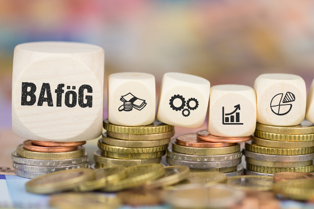 1 großer Würfel beschriftet mit BAföG und vier kleine Würfel beschriftet mit Finanzsymbolen liegen auf Euromünzstapeln (Quelle: ©magele-picture - stock.adobe.com) 1 großer Würfel beschriftet mit BAföG und vier kleine Würfel beschriftet mit Finanzsymbolen liegen auf Euromünzstapeln