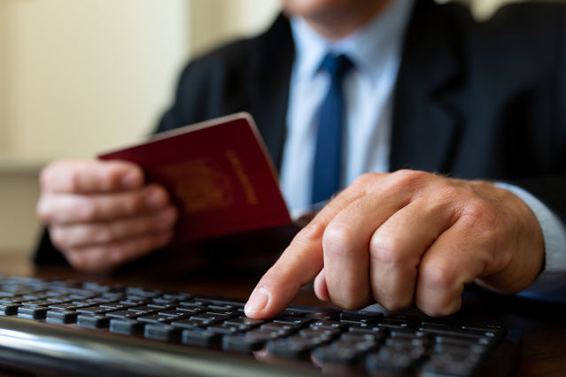 civil servant holds passport in hand and with the other hand he types on a keyboard